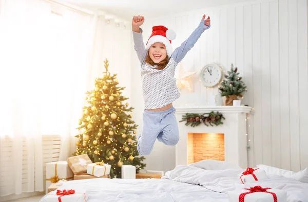 Happy child girl jumping in bed on Christmas morning — Stock Photo, Image
