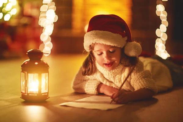 Criança menina escrevendo carta santa casa perto da árvore de Natal — Fotografia de Stock