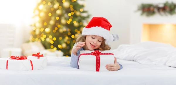 Gelukkig kind meisje met giften in bed op kerstochtend — Stockfoto