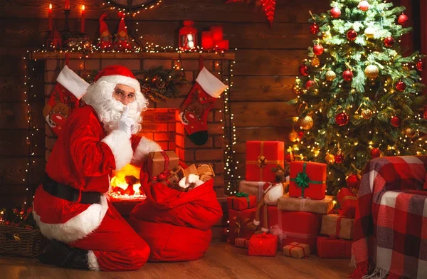 Vrolijk kerstfeest! Santa claus in de buurt van open haard en boom met cadeau — Stockfoto