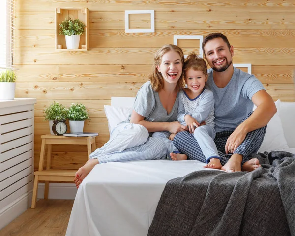 Счастливая семья мать, отец и ребенок смеется в постели — стоковое фото