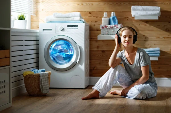 Mulher dona de casa feliz ouve música em fones de ouvido na lavanderia — Fotografia de Stock