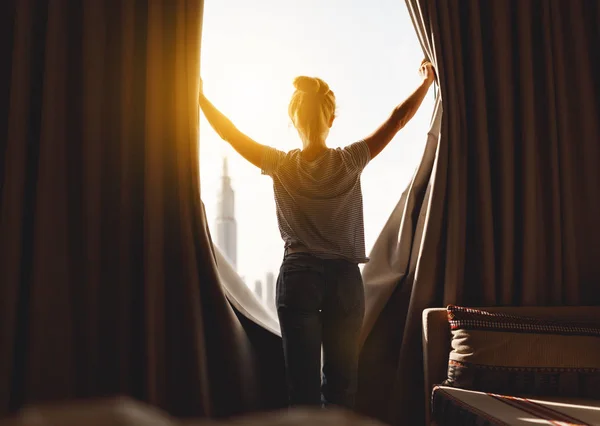 Lycklig kvinna sträcker sig och öppnar gardiner vid fönstret i morgon — Stockfoto