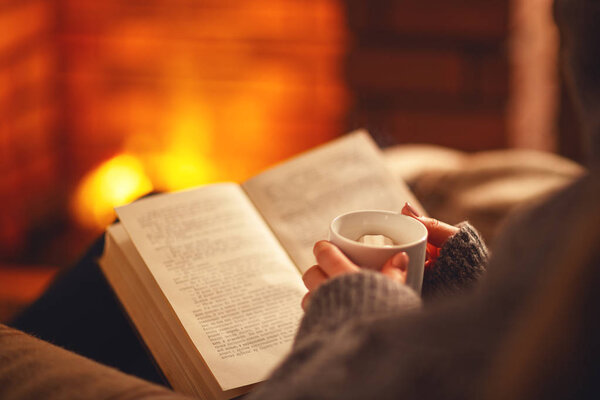 book and cup of coffee in hands of girl on  winter evening near 