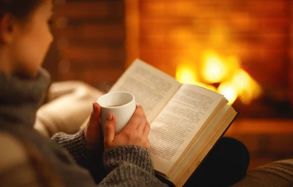 Libro y taza de café en manos de chica en la noche de invierno cerca — Foto de Stock