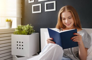Mutlu genç kadın kitap okur ve yatakta kahve içer  