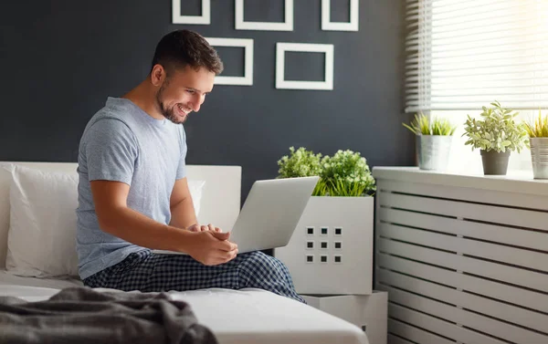 Счастливый молодой человек с ноутбуком и чашкой кофе в постели — стоковое фото