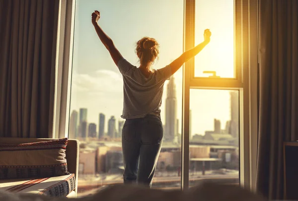 Mulher feliz se estende e abre cortinas na janela de manhã — Fotografia de Stock