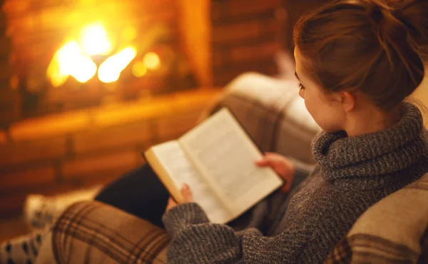 Giovane donna che legge un libro vicino al camino in una serata invernale — Foto Stock