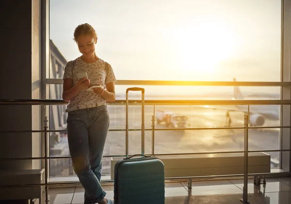 Jonge vrouw te wachten voor het vliegen op de luchthaven bij raam met suitcas — Stockfoto