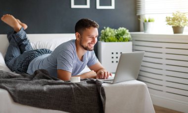 dizüstü bilgisayar ve kahve yatakta mutlu genç adam