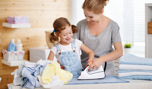 Happy family mother housewife and child daughter ironing clothes