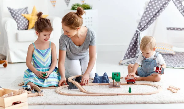 Familia madre e hijos jugar un ferrocarril de juguete en la sala de juegos — Foto de Stock