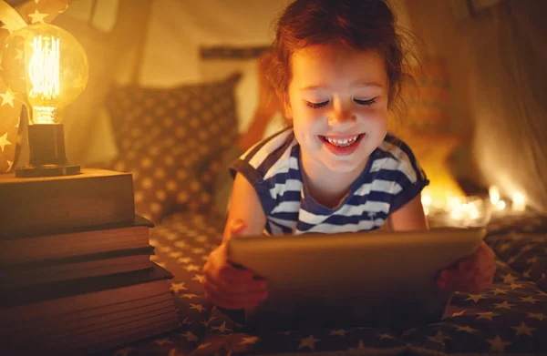 Boldog gyermek lány nevetve a sötét sátorban otthon tábla-PC — Stock Fotó
