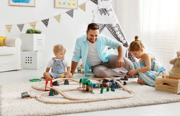 Отец и дети играют в игрушечную железную дорогу в игровой комнате — стоковое фото