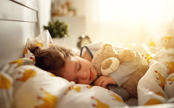 Child  girl sleeps in her bed with toy teddy bear  in morning — Stock Photo, Image