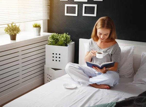 Felice giovane donna legge libro e beve caffè a letto — Foto Stock