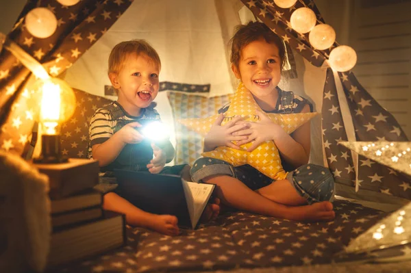 Дети мальчик и девочка читают книгу с фонариком в палатке — стоковое фото