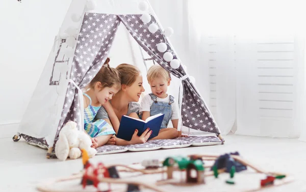 Famille mère lecture aux enfants réserver dans la tente à la maison — Photo