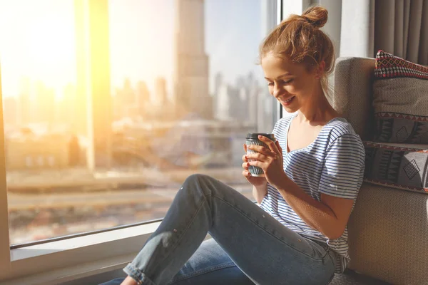 Glad ung kvinna dricker kaffe i morgon på fönster — Stockfoto