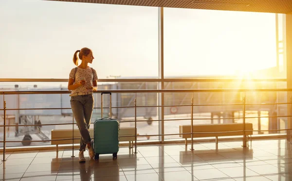 Młoda kobieta czeka na latające na lotnisko o okna z suitcas — Zdjęcie stockowe