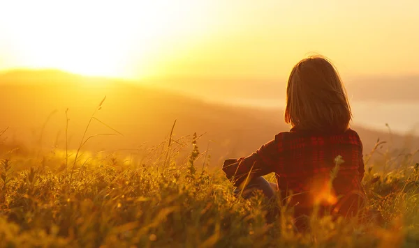 Woman sits with her back in the field and look sunset in the mou — Stock Photo, Image