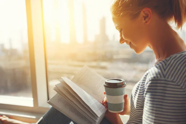 Glad ung kvinna läser bok och dricker kaffe i sängen — Stockfoto