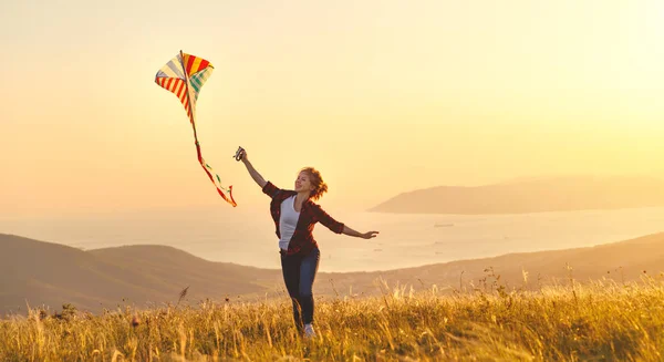 夏天日落时, 快乐的年轻女子带着风筝奔跑在空地上 — 图库照片