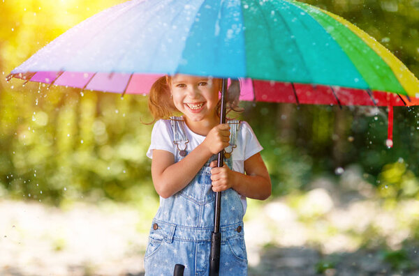 Happy child girl laughs and plays under summer rain with an umbr