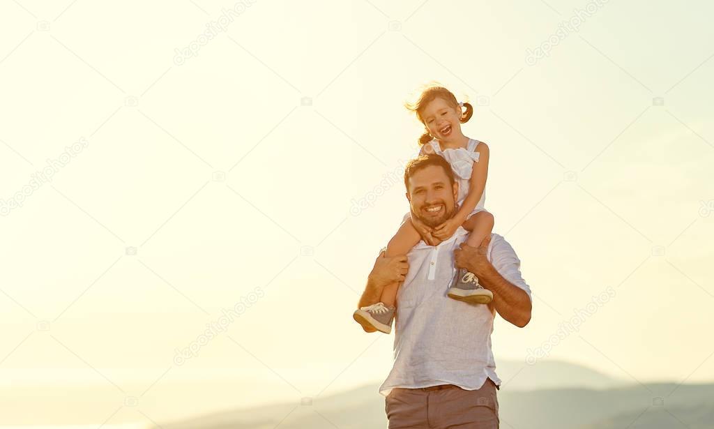 father's day. child daughter sits on her dad shoulders outdoors 