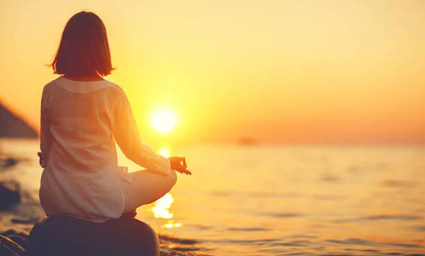 Woman practices yoga and meditates in lotus position on sunset b — Stock Photo, Image