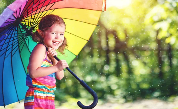 Gelukkig kind meisje lacht en speelt onder zomerregen met een umbr — Stockfoto