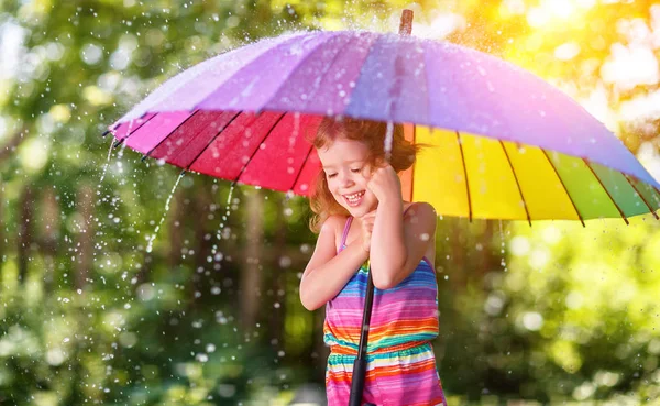 Happy child girl laughs and plays under summer rain with an umbr — Stock Photo, Image