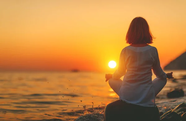 Woman practices yoga and meditates in lotus position on sunset b — Stock Photo, Image