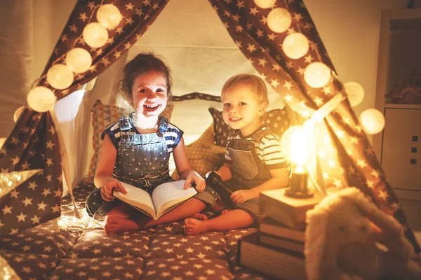 Barn pojke och flicka läsebok med ficklampa i tält — Stockfoto