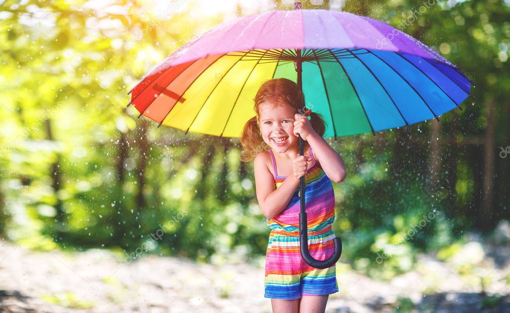 Happy child girl laughs and plays under summer rain with an umbr