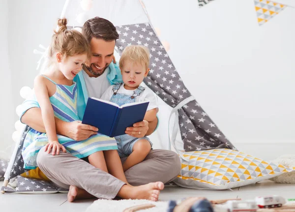 Padre de familia leyendo a los niños libro en tienda de campaña en casa — Foto de Stock