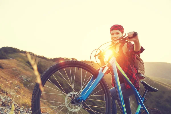 Woman tourist on a bicycle at top of mountain at sunset outdoors — Stock Photo, Image