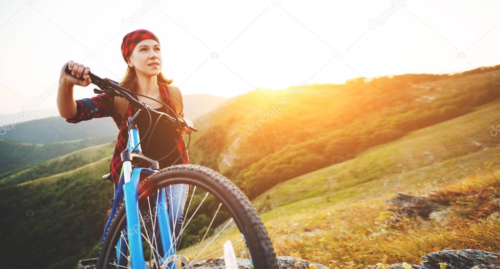 Woman tourist on a bicycle at top of mountain at sunset outdoors