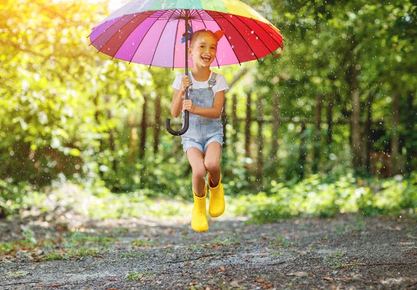 Счастливая забавная девочка с зонтиком, прыгающая на лужах в рубе — стоковое фото