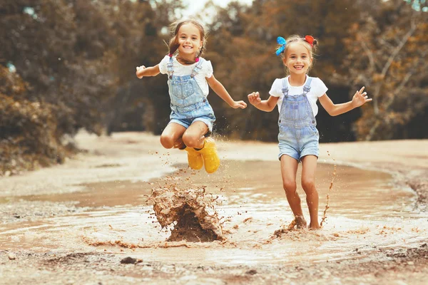 Szczęśliwy śmieszne siostry bliźniaczki dziecko dziewczynka skoki w kałużach na rub — Zdjęcie stockowe