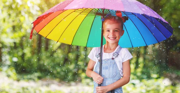 Happy child girl laughs and plays under summer rain with an umbr — Stock Photo, Image