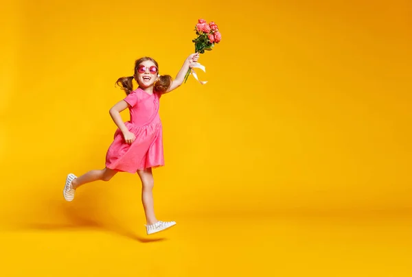 Roliga barn flicka körs och hoppar med bukett blommor på färg — Stockfoto