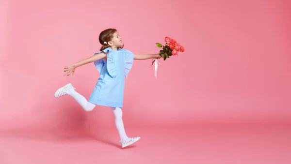 Roliga barn flicka körs och hoppar med bukett blommor på färg — Stockfoto