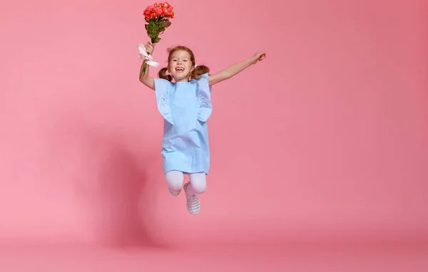 Roliga barn flicka körs och hoppar med bukett blommor på färg — Stockfoto