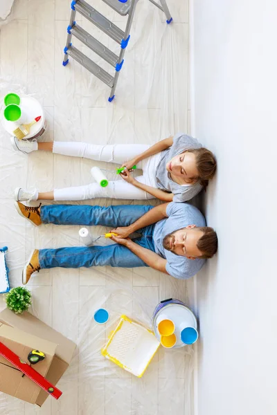Ung trött par reparerar och målning vägg vid hom — Stockfoto