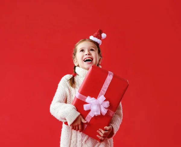 Fröhliche lustige Kindermädchen mit Weihnachtsgeschenk auf rotem Hintergrund — Stockfoto