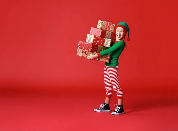 Cheerful funny child in Christmas elf costume with gifts on   re — Stock Photo, Image