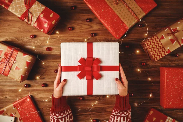 Červené vánoční dárky s rukama a věnce světel na dřevě — Stock fotografie