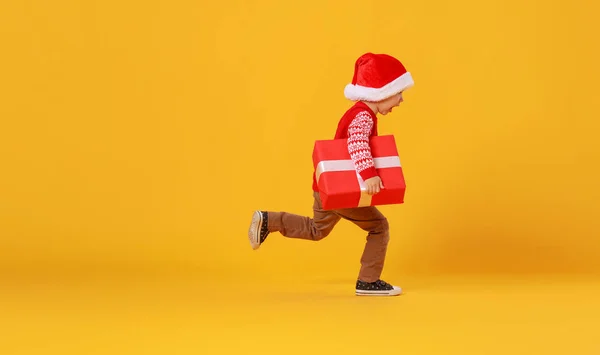 Gelukkig grappig kind jongen in rood lopen met kerstcadeau op yel — Stockfoto